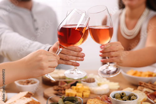 People clinking glasses with rose wine above wooden table indoors  closeup