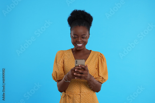 Happy young woman with smartphone on light blue background © New Africa