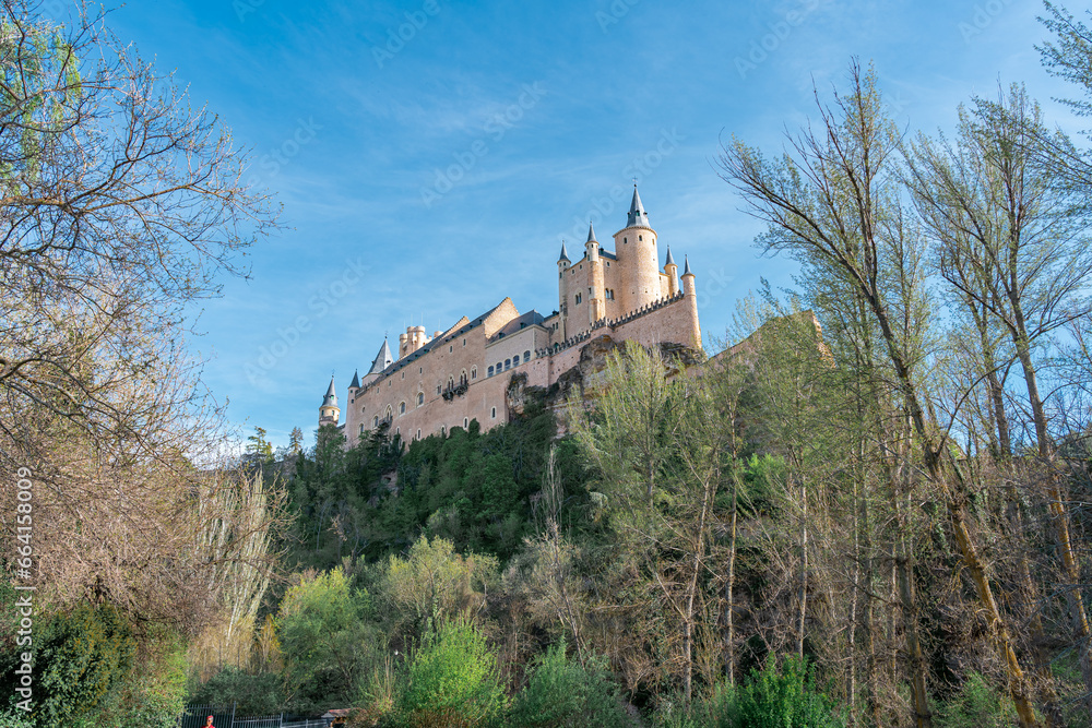 Castillo de cuento europeo en lo alto de una colina, rodeado de vegetación. El Alcázar de Segovia visto desde el mirador del valle, un día soleado con cielo azul.