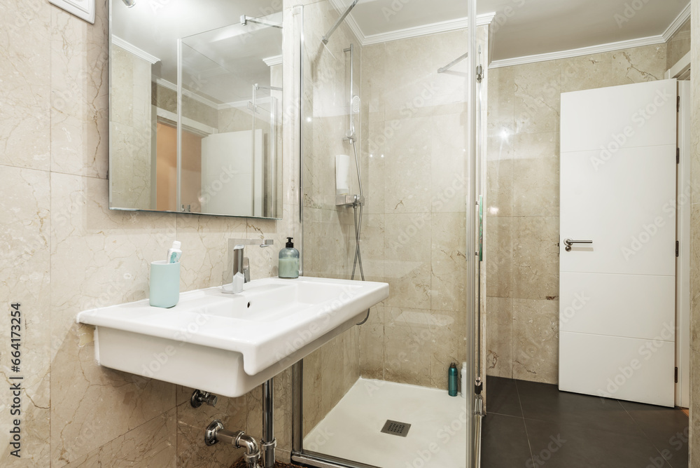 Bathroom with porcelain sink without cabinet underneath, with a mirror on the marble wall and shower cabin with glass screens Bathroom with porcelain sink without cabinet underneath, with a mirror on the marble wall and shower cabin with glass screens