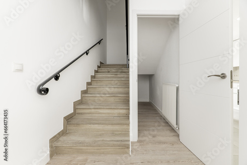 Distributor landing of a two-story single-family residential house with black metal handrails on a staircase with wooden steps and a closet in the stairwell with a white wooden door
