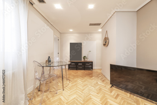 Small living room of a house with circular glass dining table with transparent methacrylate chairs and French oak parquet floors laid in a herringbone pattern photo