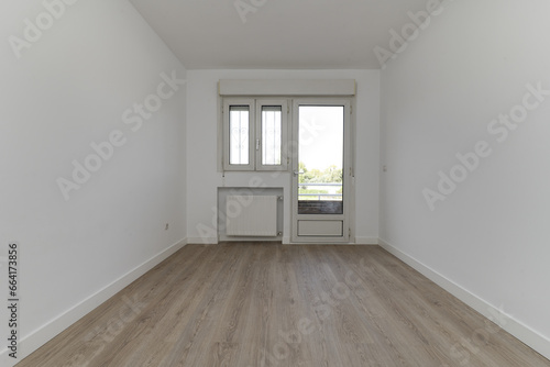 Empty bedroom with windows and access door to a terrace  an aluminum radiator in a niche and light wooden floors