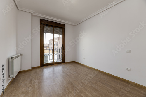 Empty room of a house with wooden floors  plaster moldings on the ceiling  a large dark aluminum and glass window and white aluminum radiator on the wall