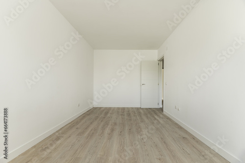 Empty room in a house with light wooden floors  a white wooden door and plain white painted walls