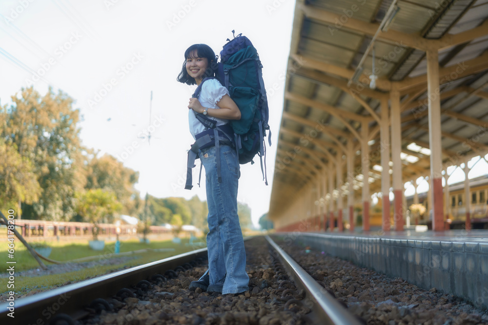 An Asian female tourist is carrying a backpack and crossing the railway tracks.
