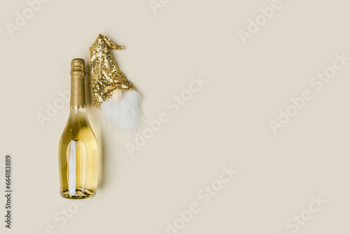 Champagne bottle and decor for bottle of wine, golden sequins hat of dwarf, Christmas and New Year holidays, festive background, copy space. Minimal style trend, beige golden colors photo