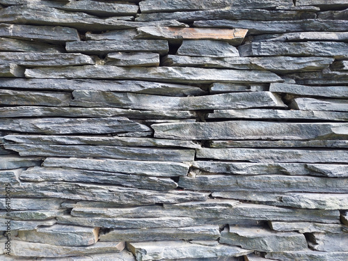 Close-up of a fence made of stacked gray stone slabs under the sun. photo