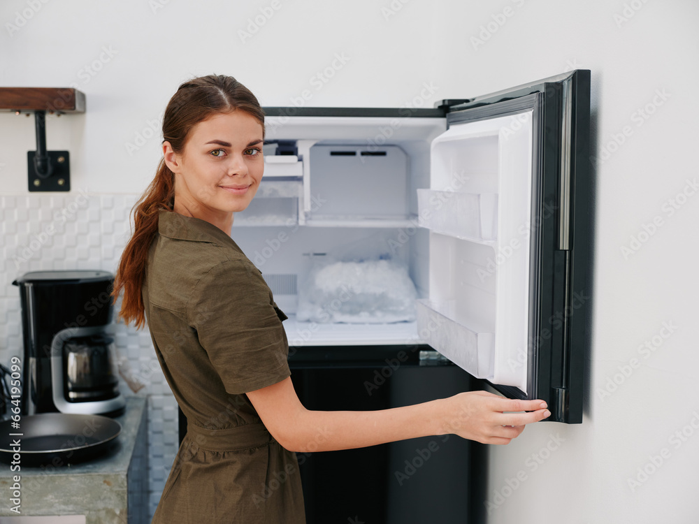 Woman smiling with teeth looking into camera in kitchen at home opened freezer empty with ice inside, home refrigerator, defrosted, view from back. Woman smiling with teeth looking into camera in kitchen at home opened freezer empty with ice inside, home refrigerator, defrosted, view from back.