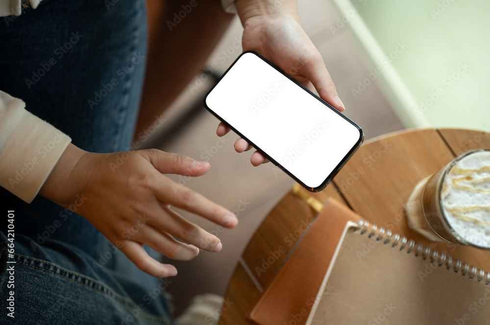 Obraz premium Top view image of a woman in casual clothes using her smartphone while relaxing in a coffee shop.