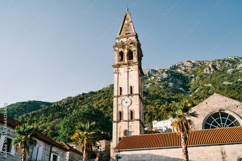 Bell tower of the Church of St. Nicholas in Perast against the backdrop of sunny green mountains. Montenegro