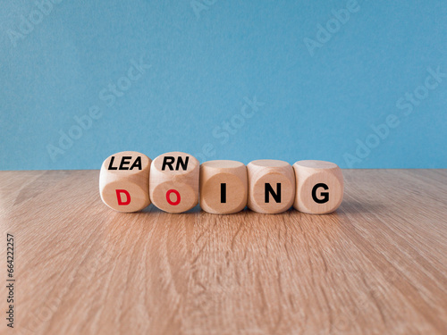 Obraz na płótnie Learning by doing concept. Turned a dice and changes the red word learning to doing, or vice versa. Beautiful wooden table blue background. Copy space. w salonie