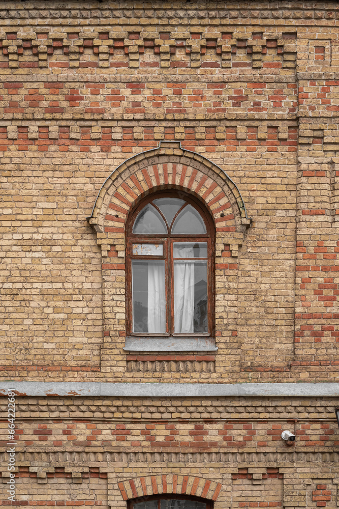 Old wooden arched brown window on an old brick wall of a 19th century building facade.