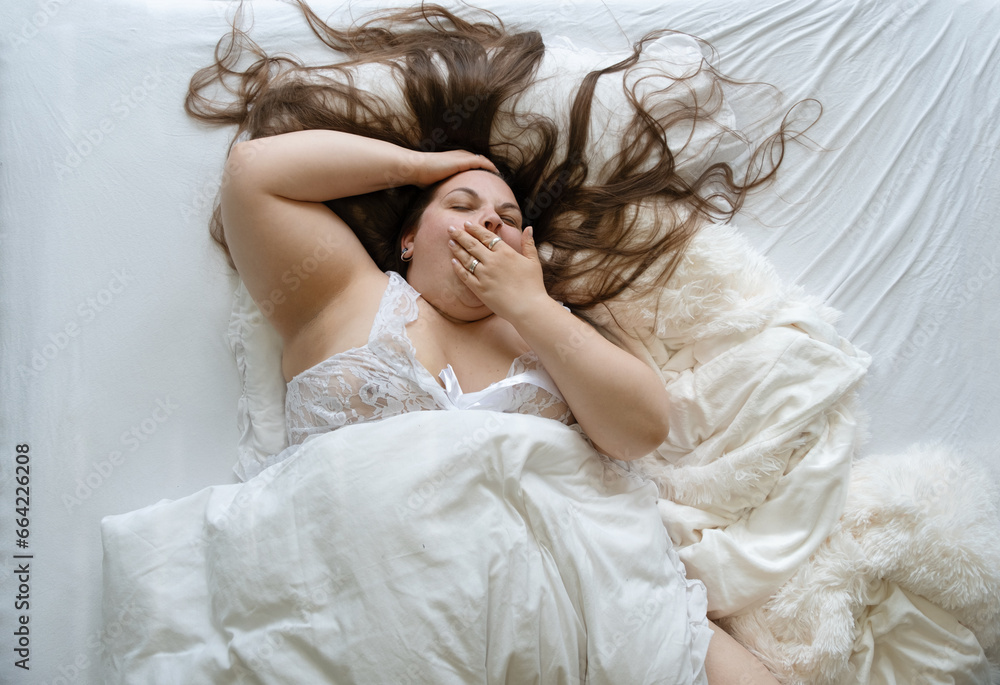 happy excited confident positive cheerful plump yawning woman with long hair in bed, brunette cute chubby plus size girl enjoying nice day, holds her hand in front of her mouth happy excited confident positive cheerful plump yawning woman with long hair in bed, brunette cute chubby plus size girl enjoying nice day, holds her hand in front of her mouth