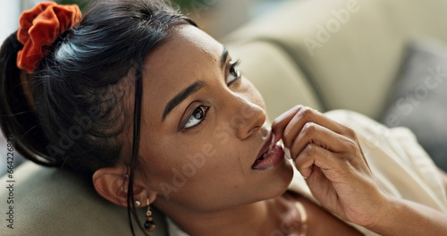 Thinking, anxiety and young woman on a sofa relaxing with an idea or memory in living room. Anxious, mental health and nervous Indian female person biting her nail in the lounge of modern apartment.