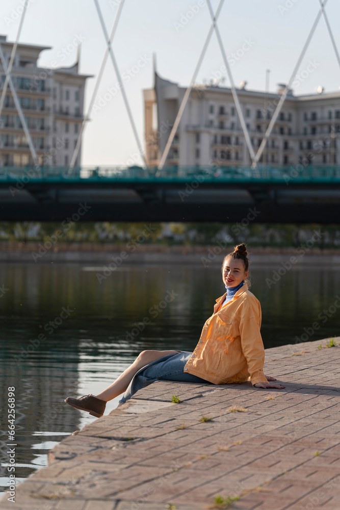 A young woman sits by the river on the embankment. Concept: freedom, enjoying life, being alone with yourself.