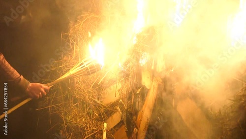 hand held close up shot of man with burning torches lighting a large wheel of fire on a midsummer night