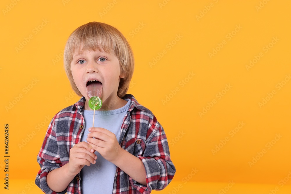 Cute little boy licking lollipop on orange background, space for text Cute little boy licking lollipop on orange background, space for text