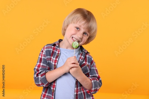 Cute little boy with lollipop on orange background