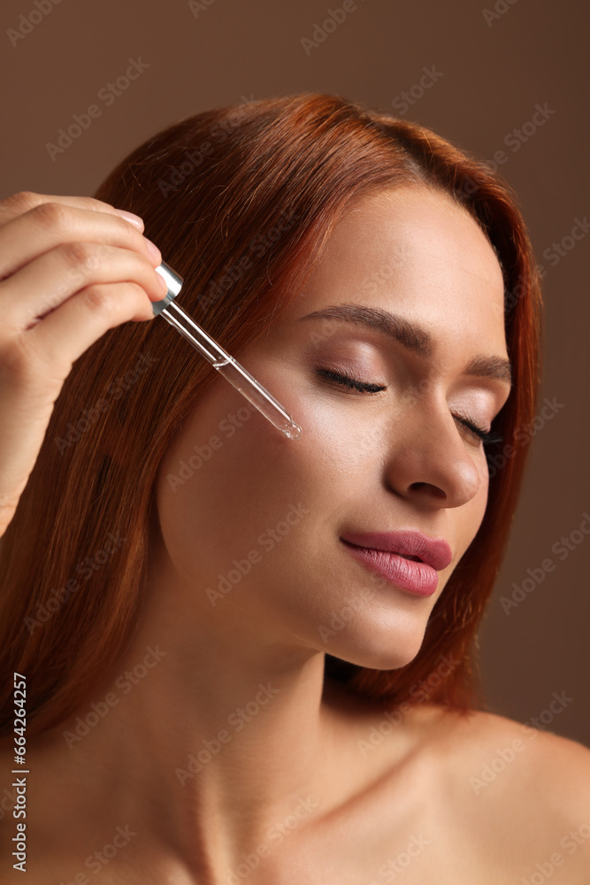Beautiful young woman applying cosmetic serum onto her face on brown background, closeup Beautiful young woman applying cosmetic serum onto her face on brown background, closeup