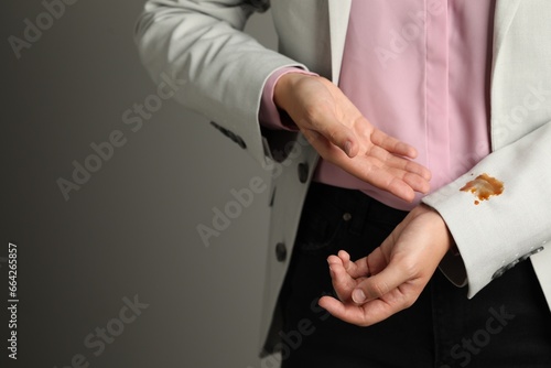 Woman showing stain of coffee on her jacket against grey background, closeup. Space for text