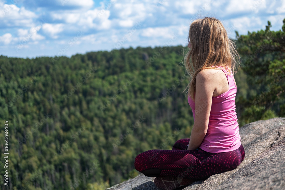 A woman does yoga. A happy woman meditates on the top of a mountain. Looks at the beautiful forest and clouds from a height. Motivation and inspiring physical training. A healthy lifestyle in nature. A woman does yoga. A happy woman meditates on the top of a mountain. Looks at the beautiful forest and clouds from a height. Motivation and inspiring physical training. A healthy lifestyle in nature.