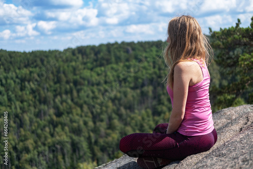 A woman does yoga. A happy woman meditates on the top of a mountain. Looks at the beautiful forest and clouds from a height. Motivation and inspiring physical training. A healthy lifestyle in nature.