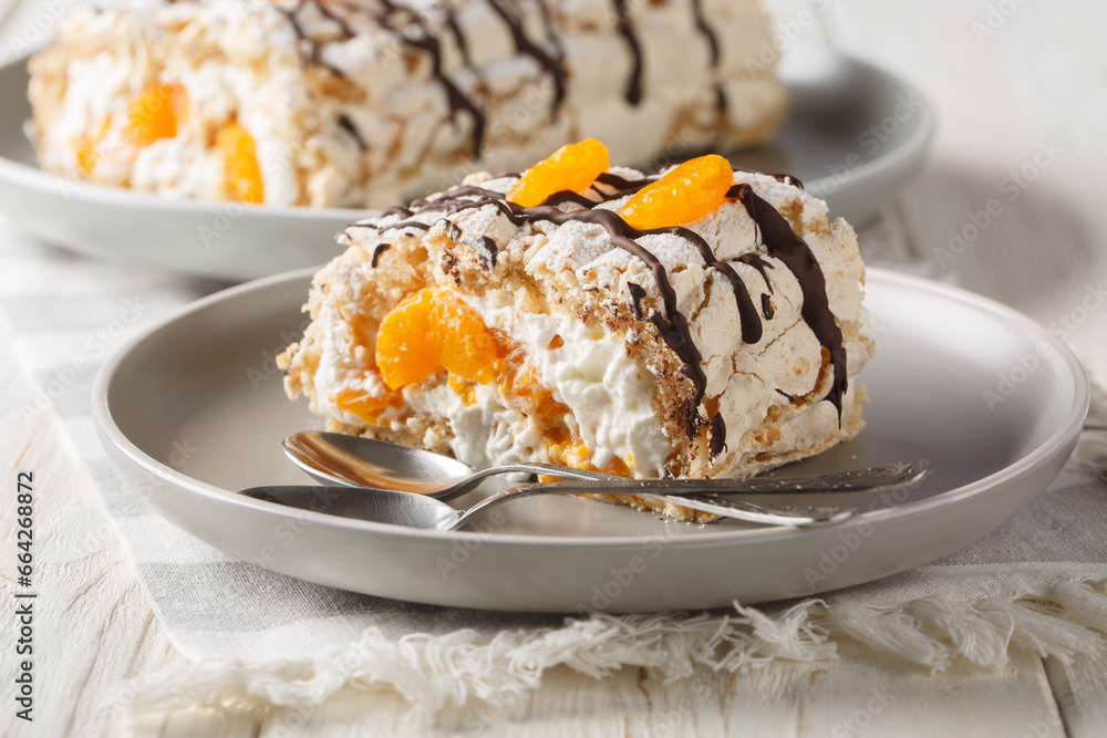 Swedish Budapest roll with hazelnut meringue and mandarins closeup on the plate on the table. Horizontal Swedish Budapest roll with hazelnut meringue and mandarins closeup on the plate on the table. Horizontal