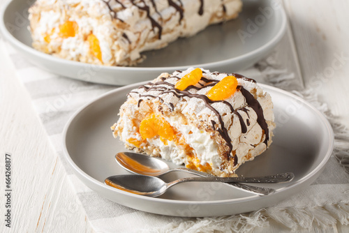 Delicious homemade Swedish dessert Budapest roll cake filled with whipped cream and tangerines close-up in a plate on the table. Horizontal