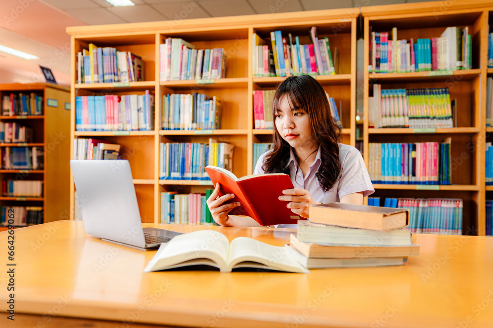 Asian female university student sitting at table with books and laptop in library Asian female university student sitting at table with books and laptop in library
