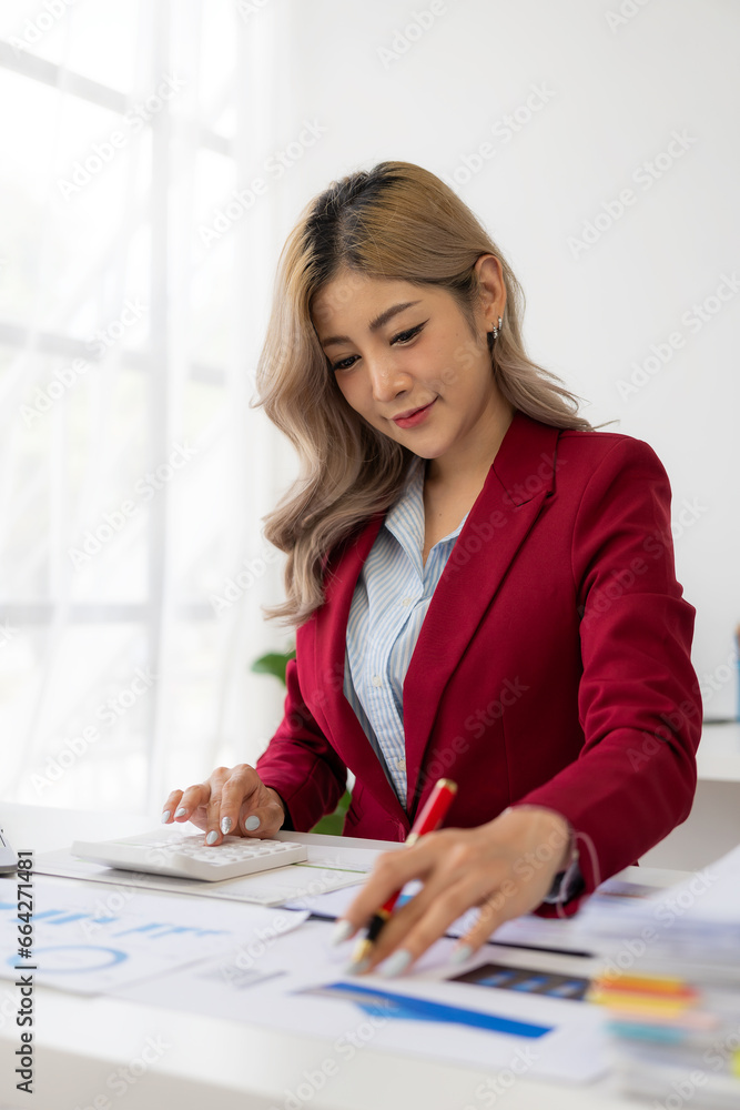 Asian female financial analyst or accountant uses laptop to work on financial audit and budgeting using calculator, checking balance sheet, working with company quarterly report. Vertical image Asian female financial analyst or accountant uses laptop to work on financial audit and budgeting using calculator, checking balance sheet, working with company quarterly report. Vertical image