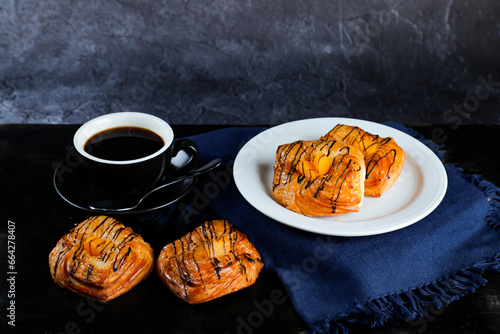 Peach Danish pastry puff served in plate with cup of black coffee isolated on napkin side view of french breakfast baked food item on grey background