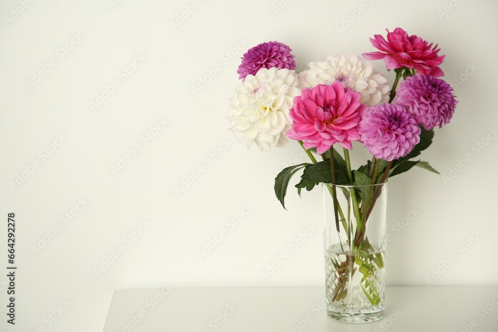 Bouquet of beautiful Dahlia flowers in vase on table near white wall, space for text