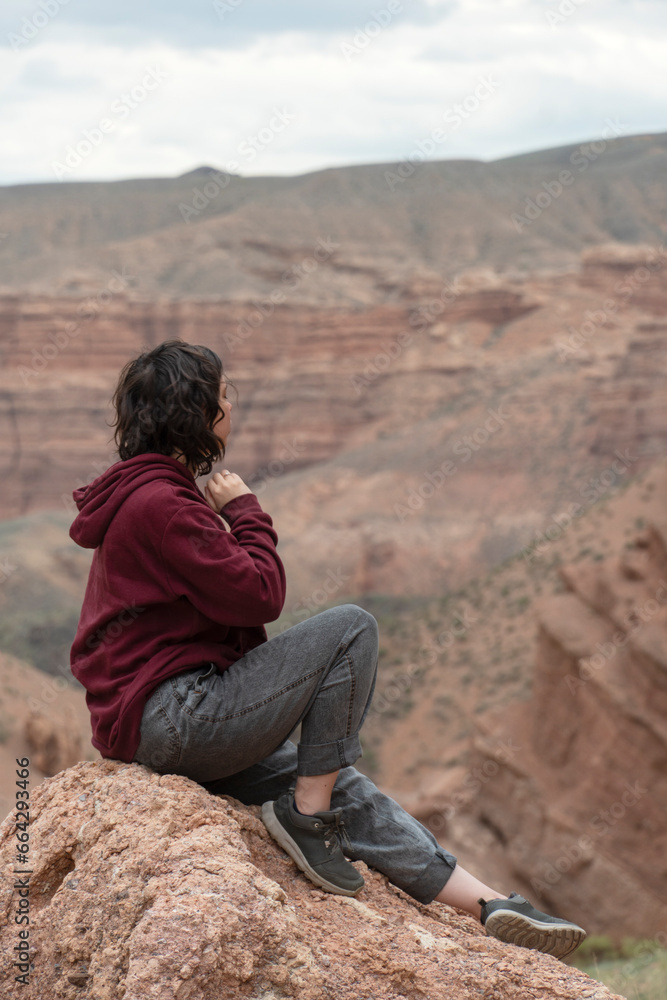 A young woman sits on a rock in the Central Asian Canyon, Charyn, Kazakhstan