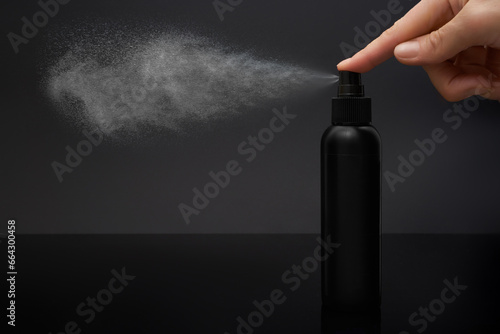 Close-up view of human hand and black spray bottle isolated on black