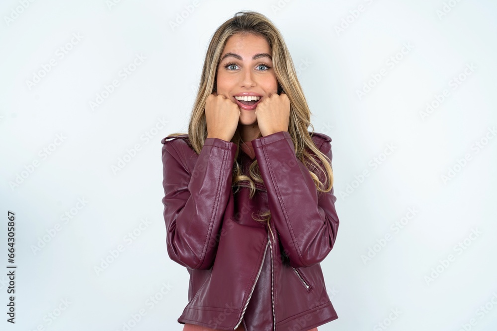 Happy Beautiful caucasian woman wearing leather jacket keeps fists on cheeks smiles broadly and has positive expression being in good mood