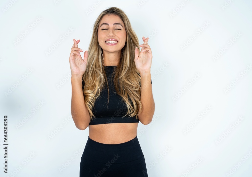 Young beautiful woman wearing sport clothes has big hope, crosses fingers, believes in good fortune, smiles broadly. People and wish concept Young beautiful woman wearing sport clothes has big hope, crosses fingers, believes in good fortune, smiles broadly. People and wish concept