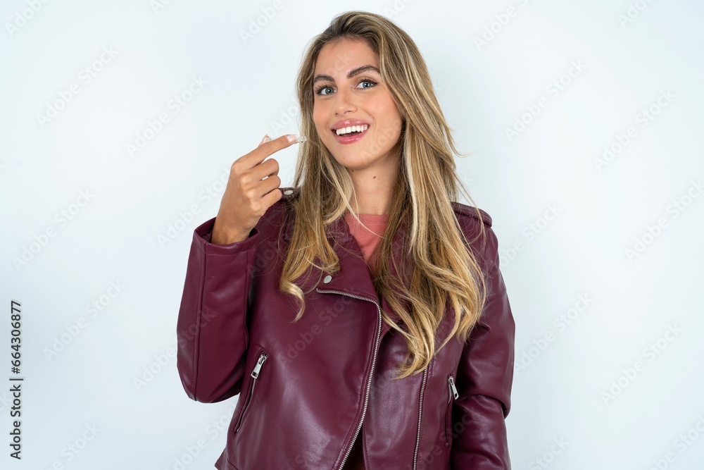 Beautiful young woman wearing jacket holding an invisible aligner ready to use it. Dental healthcare and confidence concept. Beautiful young woman wearing jacket holding an invisible aligner ready to use it. Dental healthcare and confidence concept.