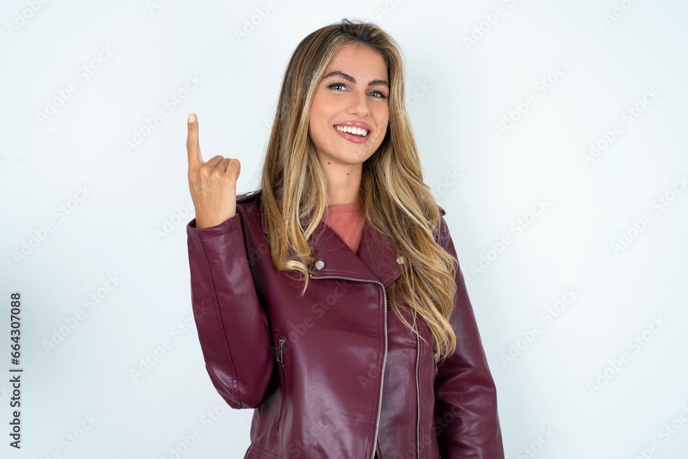 Beautiful young woman wearing jacket smiling and looking friendly, showing number one or first with hand forward, counting down Beautiful young woman wearing jacket smiling and looking friendly, showing number one or first with hand forward, counting down