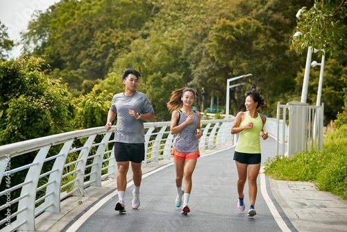 Canvas Print three young asian adults running jogging outdoors in park
