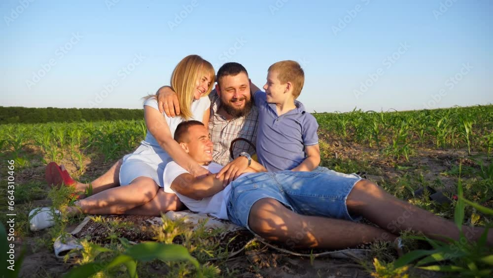 Young parents with two sons spending time together at corn meadow. Mommy and daddy with children sitting on green field and enjoying beautiful nature. Concept of a family happiness. Slow motion Young parents with two sons spending time together at corn meadow. Mommy and daddy with children sitting on green field and enjoying beautiful nature. Concept of a family happiness. Slow motion
