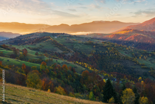 carpathian countryside at sunrise in autumn. rural fields and forested hill in morning light. distant ridge beneath a sky with clouds