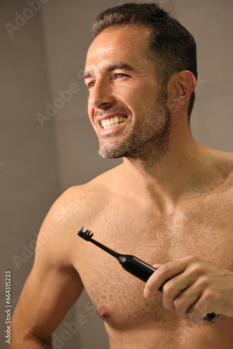 Przystojny, dojrzały mężczyzna myje zęby. A man brushes his teeth with an electric toothbrush.