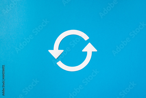Recycling symbol cut out of white paper on blue background, top view. Concept of ecology and paper recycling. Recycled. Eco arrow reuse material.