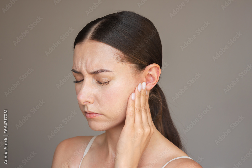 Caucasian brunette woman is experiencing acute pain in her ear. She frowns, closes her eyes, presses her ear with her fingers. Suffers from otitis. Caucasian brunette woman is experiencing acute pain in her ear. She frowns, closes her eyes, presses her ear with her fingers. Suffers from otitis.