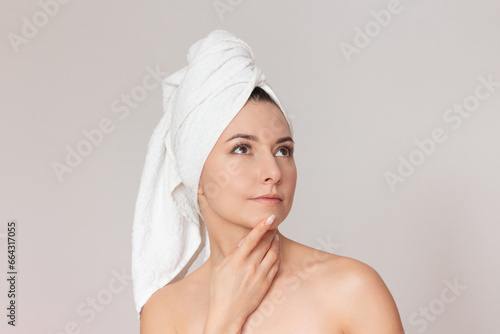a young caucasian pretty naked woman with a towel on her head looks up thoughtfully, touching her chin with her finger. Isolated on a light background. Copy space