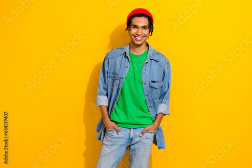 Photo of confident attractive man wear jeans shirt red hat smiling walking isolated yellow color background