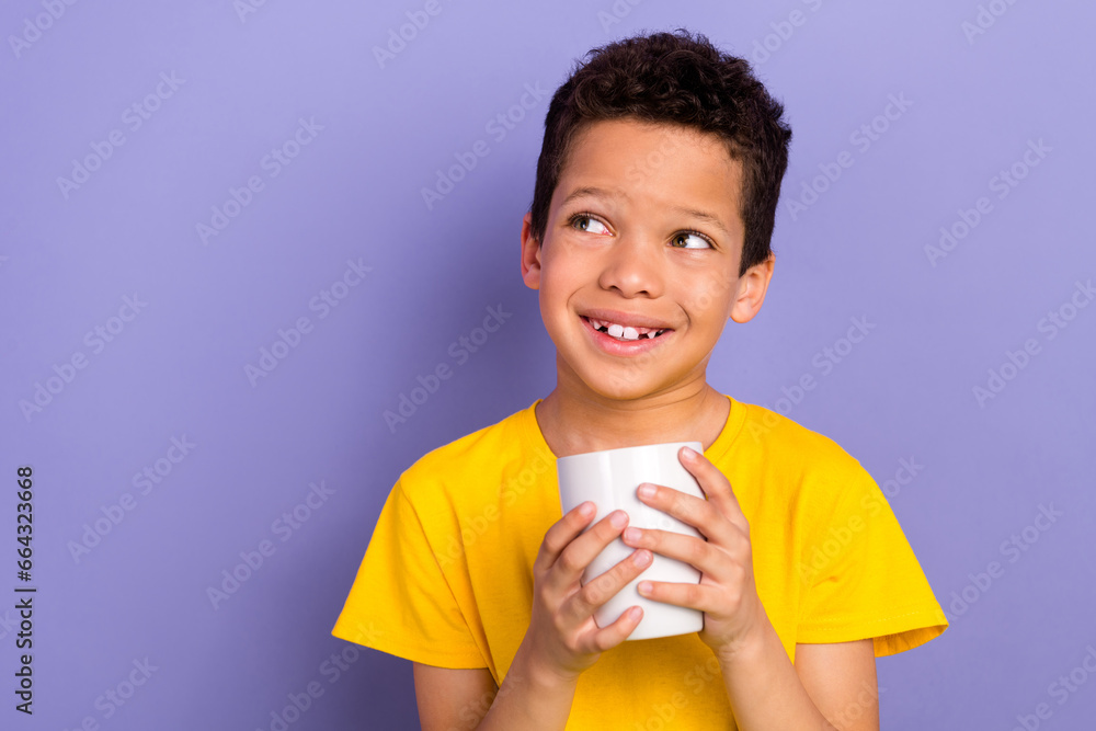 Photo of beautiful nice boy son wear yellow trendy clothes hand hold cup look up offer empty space isolated on purple color background Photo of beautiful nice boy son wear yellow trendy clothes hand hold cup look up offer empty space isolated on purple color background