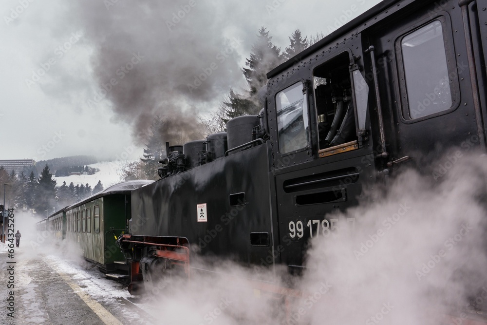 Vintage steam locomotive chugging down a set of railroad tracks, emitting plumes of smoke
