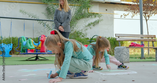 Kindergarten teacher watches the girls draw with chalk. Children art.